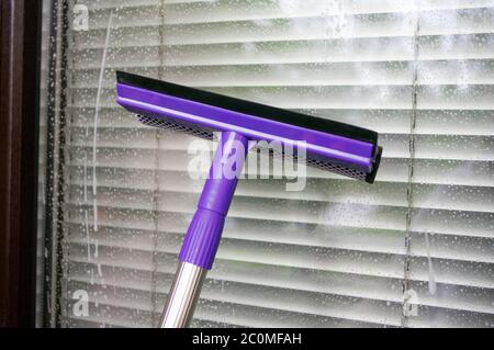 Cleaning window using a violet squilgee to wash glass. Housekeeping concept. Stock Photo