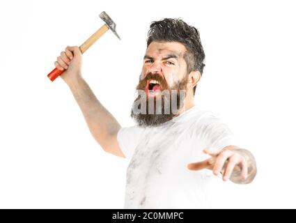 Mad repairman concept. Builder, plasterer, repairman, foreman attaks with hammer in hand, white background. Man with shouting face looks mad. Man with beard in dirty dusty shirt. Stock Photo