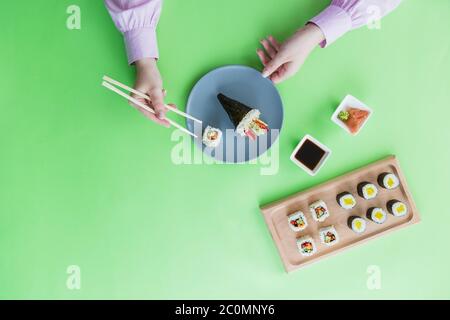 Flat lay of female hand using chopsticks for eating sushi rolls set. Stock Photo
