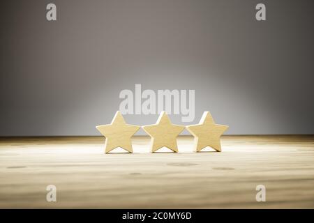 Three star rating: three wooden stars in a row on a wooden table with gray background. Selective focus. Concept shot for rating / reviews. Stock Photo