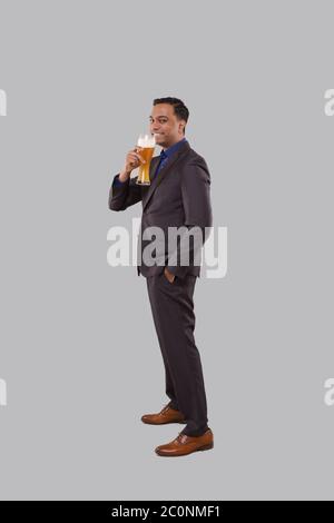 Businessman Drinking Beer from Glass. Indian Business man Standing Full Length with Beer in Hand Stock Photo