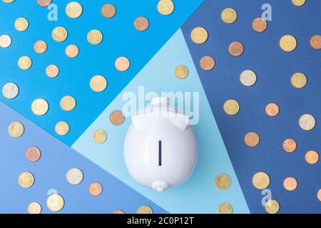 White piggy bank with many euro coins around viewed from above with a cool colored background made from card stock Stock Photo