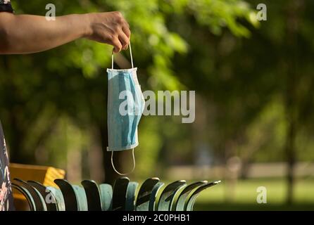 Close-up of a hand, mask and trash bin at outdoors. Girl in the park throws a medical mask into the bin. Rest at nature. Fresh air. Stock Photo