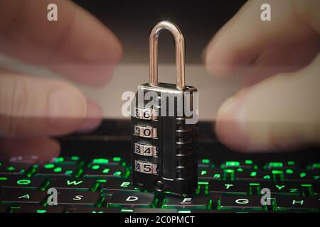 Hands trying to open combination Code Padlock on green backlit laptop keyboard. Double exposure. Cyber crime concept. Stock Photo