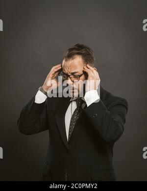 Pensive businessman rubs his head trying to concentrate or feels headache in stress from excessive work. Intelligent man on gray background. Copy Stock Photo