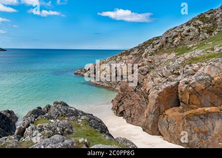 ACHMELVICH BAY AND BEACH SUTHERLAND HIGHLANDS SCOTLAND A SMALL COVE WITH BLUE  SKY WHITE SAND AND ORANGE COLOURED ROCKS Stock Photo