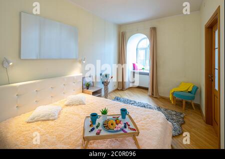 Modern interior of luxury bedroom in apartment. Tray with breakfast on the bed. Arch window. Pillows on the sill. Stock Photo