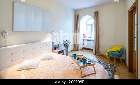 Modern interior of luxury bedroom in apartment. Tray with breakfast on the bed. Arch window. Pillows on the sill. Stock Photo