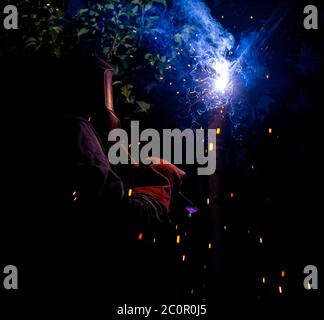 Worker with protective mask welding metal and producing smoke and sparks. arc welding Stock Photo