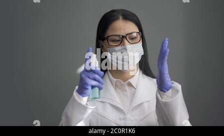 Doctor disinfects hands with an antiseptic. Asian female medical worker sprinkles an antiseptic on her hands in rubber gloves standing in office Stock Photo