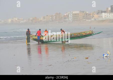 A group of artisanal fishers pushing a pirogue in Yoff beach, Dakar, Senegal Stock Photo