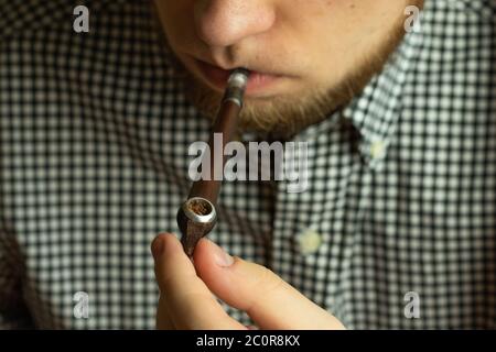 Bearded man with a pipe smoking tobacco in his mouth. Stock Photo