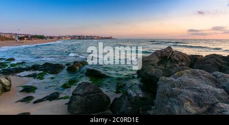 idyllic sunset on the sea shore. waves crashing rocks on sandy beach. beautiful cloudscape above the horizon Stock Photo