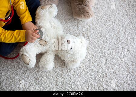 Sweet toddler child, playing doctor, examining teddy bear toy at home, isolated background Stock Photo