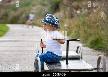 Adorable toddler boy, riding old retro car with four wheels in a village Stock Photo