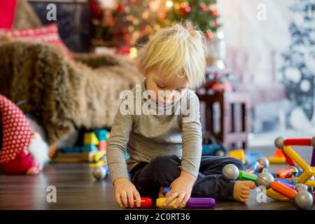 Sweet blonde toddler boy, playing with plastic construction, making different shapes, christmas decoration around him Stock Photo