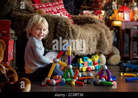 Sweet blonde toddler boy, playing with plastic construction, making different shapes, christmas decoration around him Stock Photo