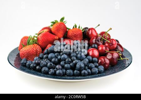 A blue patterned plate with blueberries, strawberries, and cherries on a white background. Stock Photo