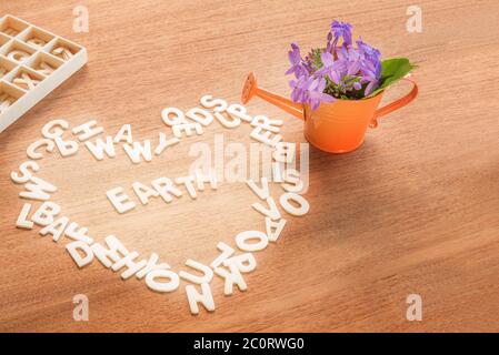 love and save the world concept, wooden alphabet formed heart shape with the word earth inside anda  watering can with flowers on a wood table backgro Stock Photo