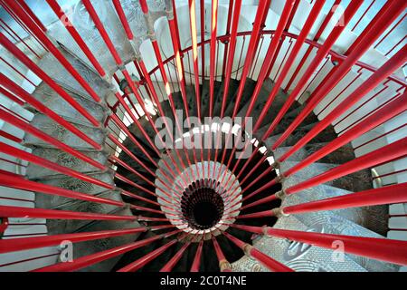 View down the steel double helix spiral staircase at the Ljubljana Castle tower with red bar posts and ornate steps Stock Photo