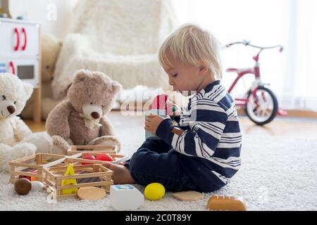 Sweet toddler boy, playing with teddy bears and wooden toys from kids kitchen set on the floor at home Stock Photo