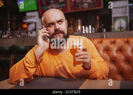 Mature man talking on the phone while drinking beer at the pub Stock Photo