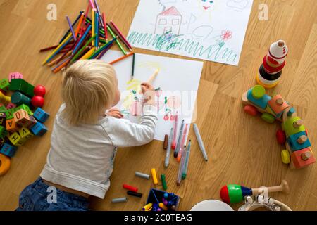 Little blonde toddler boy, drawing with pastels and coloring pens, playing with early development wooden toys Stock Photo