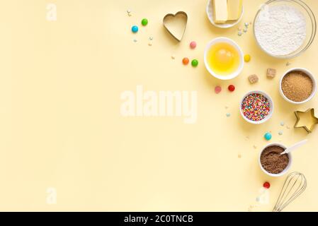 Baking utensils and ingredients.  Eggs, flour, sugar sprinkling, whisk with cookie cutters on  yellow background. Baking concept flat lay, copy space. Stock Photo