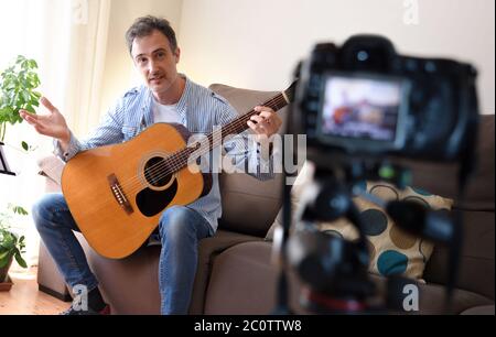 Video Blogger doing a review of a guitar with a camera recording in his living room Stock Photo