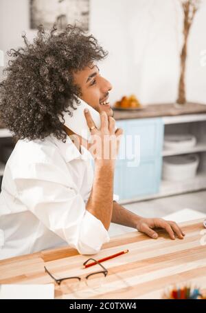 Handsome man talking mobile phone. Side view of cute Arab guy communicates by smart phone with friends or clients working remotely. Work from home Stock Photo