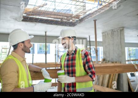Building workers in yellow vests and gloves having coffee break Stock Photo