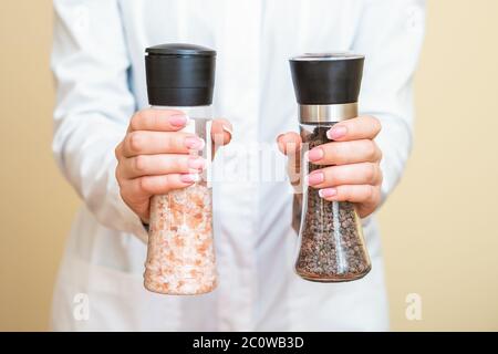 Female hands holding salt and pepper mills wearing white shirt on yellow background. Stock Photo