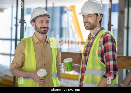 Building workers in yellow vests and helmets having coffee break Stock Photo