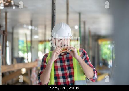Building worker in yellow vest and helmet eating sandwich Stock Photo