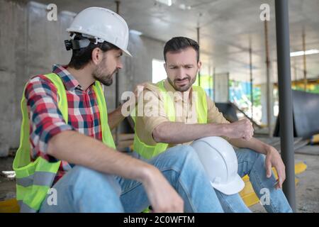 Building worker putting his hand on shoulder of his demotimated coworker, trying to support him Stock Photo