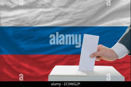 man putting ballot in a box during elections in russia in front of flag Stock Photo