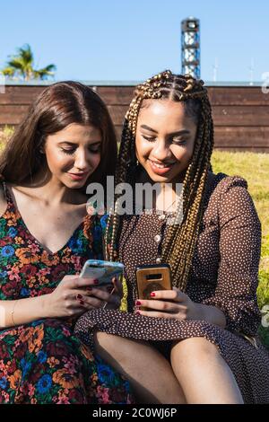 Multiethnic friends watching videos on a smartphone - Girlfriends laughing and having fun outdoors Stock Photo