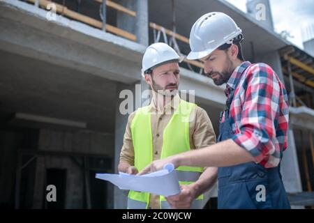 Building workers standing in front of crane, checking blueprint, brainstorming Stock Photo