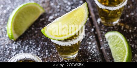 small glass of tequila, fiery drink from mexico. Lemon, coarse salt on wooden background. Stock Photo