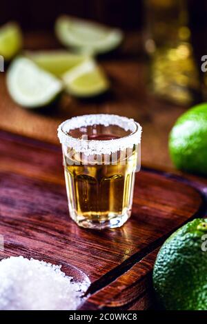 glass of tequila, on wooden table, with lemons and salt in the background. fiery drink with vodka Stock Photo