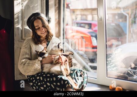 Attractive girl embracing her Siamese cats. Indoor portrait of cute woman playing with her two pets. Stock Photo