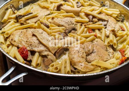 Cooking creamy Italian chicken marsala with King oyster mushrooms and sundried tomatoes served with penne rigate pasta Stock Photo