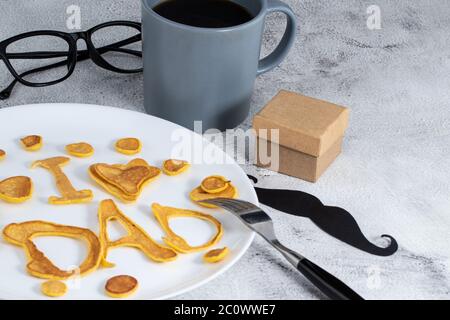 Celebrating Father's Day. Breakfast: pancakes in form of congratulations - I love dad , and coffee mug and . copy space. Stock Photo