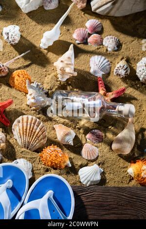 A glass bottle corked with a letter inside was on one of the sea wild beaches. Beach slippers. Stock Photo