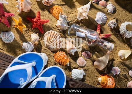 A glass bottle corked with a letter inside was on one of the sea wild beaches. Beach slippers. Stock Photo