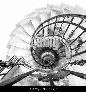 Upside view of indoor spiral winding staircase with black metal ornamental handrail. Architectural detail in St. Stephen's Basilica in Budapest, Hungary. Black and white image. Stock Photo