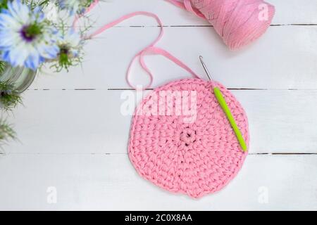 Crocheting and home hobby concept. Top view of crochet work with crochet hook and pink yarn on white wooden table Stock Photo
