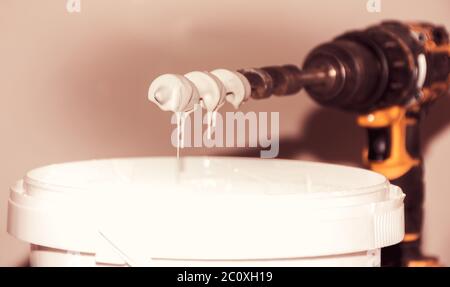 white wall paint mixed with electric hand tool, paint flowing down from the mixer bit. closeup. Stock Photo