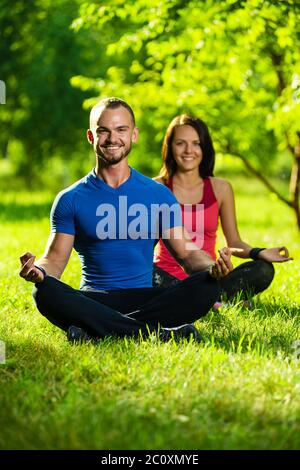 Young man and woman doing yoga in the sunny summer park Stock Photo