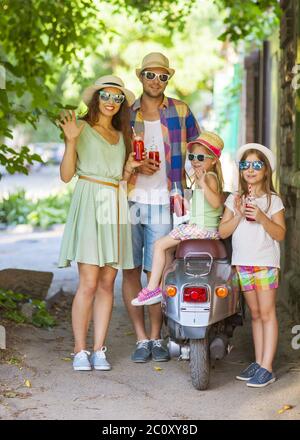 Happy young family with a vintage scooter in the street wearing hats sunglasses Stock Photo